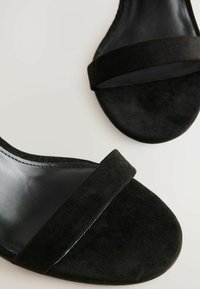 Sandales en suède noir avec un design à double sangle, doublure en cuir lisse et semelle plate avec des détails de couture subtils.