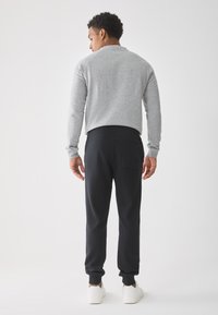 Gray long-sleeve sweatshirt with a relaxed fit, paired with black tapered sweatpants and white sneakers, viewed from behind.