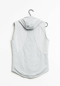 Sudadera sin mangas de color gris claro con un respaldo texturizado, que presenta una pequeña capucha y bolsillos laterales, colgada en un gancho negro sobre un fondo blanco.
