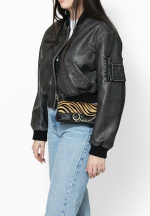 Giacca bomber in pelle nera con polsini a costine e molteplici tasche con zip. Piccola borsa nera a righe zebrate con tracolla a catena.