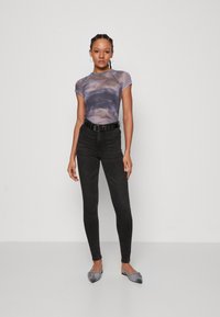 Fittet lilla tie-dye topp med korte ermer, kombinert med svarte høyt midje jeans og grå flate sko. Minimalistisk svart beltedetalj.