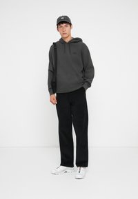 Hanorac gri cu buzunar frontal și șnur, pantaloni largi negri, adidași albi și o șapcă gri cu un logo brodat.