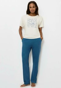 Kremowa bluzka z krótkim rękawem w niebieski kwiatowy wzór, zestawiona z niebieskimi spodniami o prostym kroju. Materiał wydaje się miękki i wygodny.