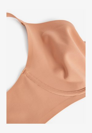 Coque de soutien-gorge couleur nude sans couture avec bretelle fine réglable et texture de tissu lisse sur fond blanc.