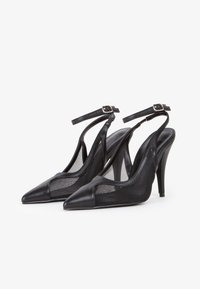 Zapatos de tacón alto negros con tiras traseras, que cuentan con una puntera puntiaguda, paneles de malla y detalles de cuero, correa ajustable en el tobillo y una silueta elegante.