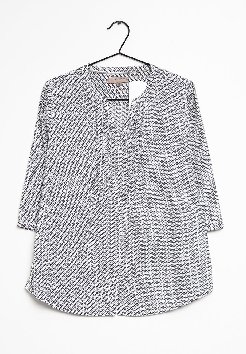 Blouse blanche boutonnée avec motif étoile géométrique noire, manches trois-quarts et légères fronces à l'avant, suspendue sur un cintre noir.
