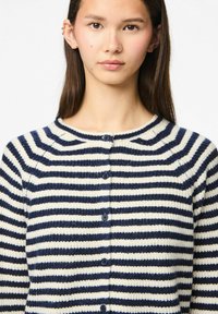 Crème en marine gestreepte cardigan gemaakt van textuurgebreid materiaal, met een ronde halslijn, knoopsluiting en horizontale strepen over de stof.