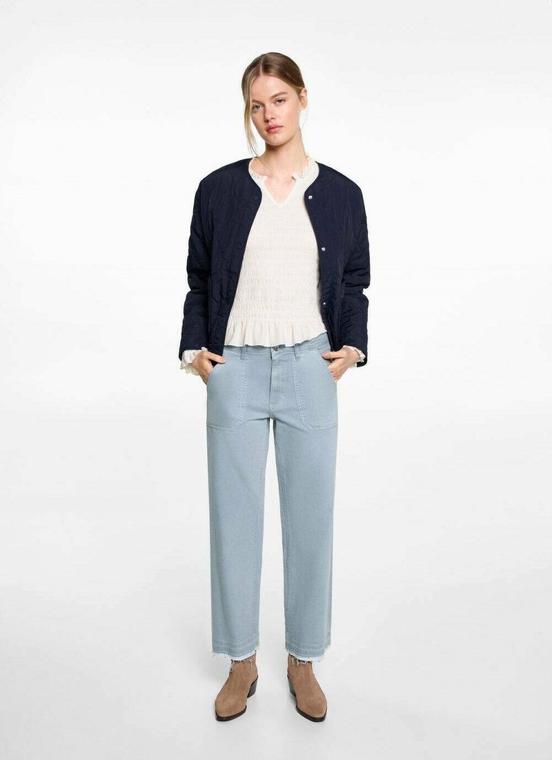 Námornícky prešívaný bomber sako, biela textúrovaná blúzka s riaseným výstrihom, svetlomodré široké nohavice a pieskové členkové čižmy.