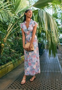 Maxi suknelė su gėlių raštu pastelinėmis spalvomis, su raukiniais rankovėmis ir prigludusia juosmens linija. Austa delninė ir plokščios basutės užbaigia įvaizdį.