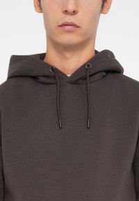 Dark gray hoodie made from soft, textured fabric. Features a drawstring hood with black ends and a relaxed fit. Simple and functional design.