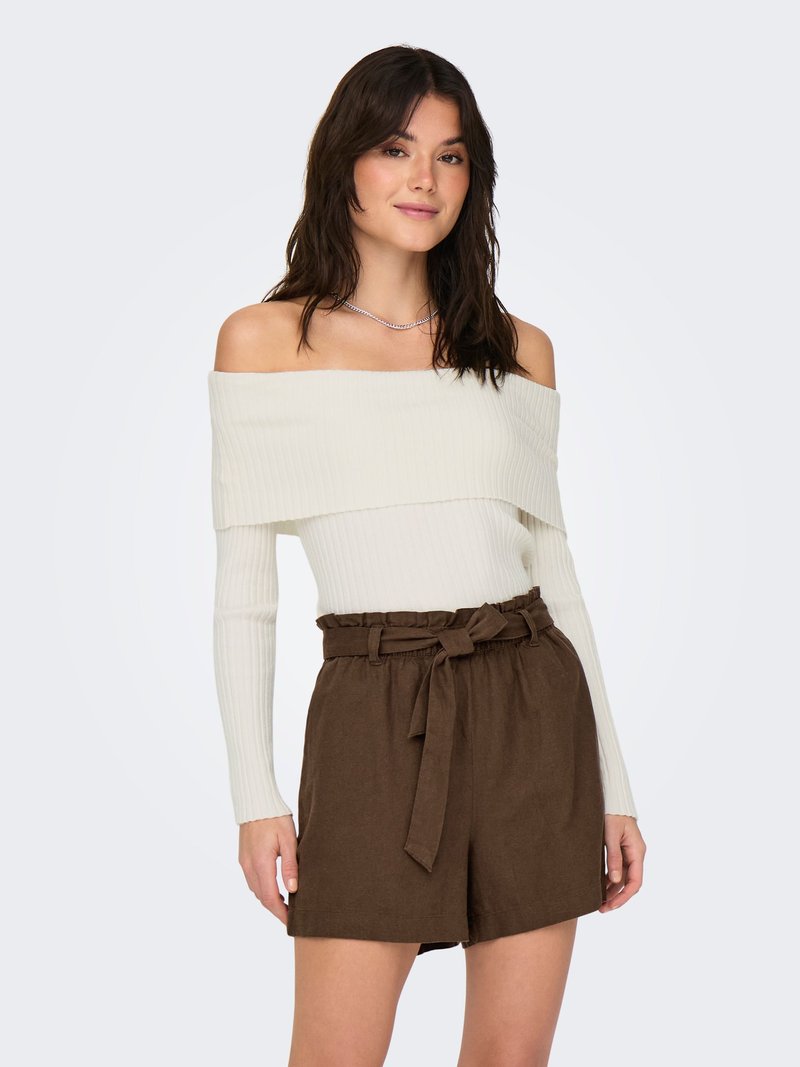 Femme portant un pull blanc côtelé épaules dénudées et un short paperbag marron taille haute avec ceinture nouée, debout devant un fond uni.