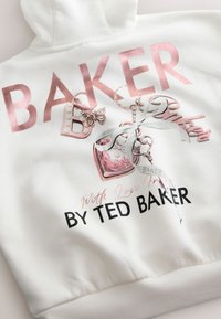 Balta džemperio su gobtuvu su metalizuotais rožinės spalvos užrašais „BAKER“ ir „BY TED BAKER“. Detalus grafikos dizainas su drugelio ir rankinės motyvais, minkšta tekstūra.