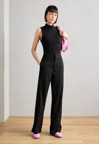 Čierny bezrukávový rolák, široké čierne nohavice s vysokým pásom a ružové slip-on topánky, doplnené ružovou taškou.