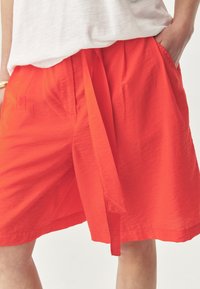 Rode, lichtgewicht shorts met een strikband in de taille, voorzien van twee zijzakken en een relaxte pasvorm. De stof heeft een zachte, licht gekreukte textuur.