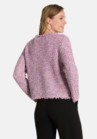 Texturiertes, gestricktes lila Sweatshirt mit lockerer Passform, ausgefranstem Saum und Knopfdetail hinten, kombiniert mit schwarzen Hosen.