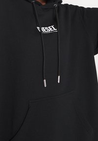 Schwarzer Kapuzenpullover aus weichem Stoff. Verfügt über eine Fronttasche, Kordeln mit Metallspitzen und ein weißes "DIESEL"-Logo auf der Brust.