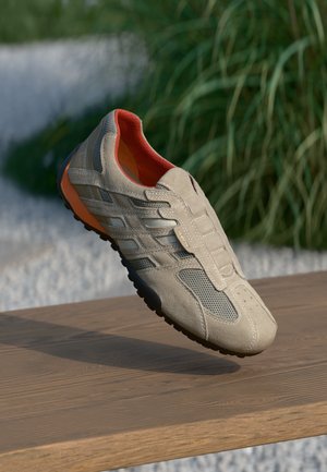 Încălțăminte sport bej, realizată din materiale din plasă și suede, cu interior portocaliu și talpă din cauciuc negru. Are șase orificii pentru șireturi și modele texturate.