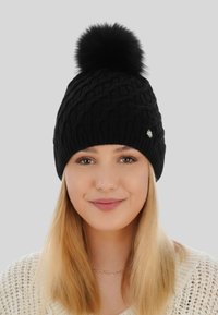 Berretto lavorato a maglia nero con un motivo a treccia texture e decorato con un morbido pom-pom nero, accentuato da un piccolo emblema argenteo.