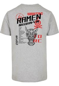 Pilka trumpa rankovė t-shirt su juodu grafiniu užvaizdžiu, vaizduojančiu kaukėtą veidą, ir raudona tekstu, kuriame pateikiamos recepto detalės bei prekės ženklo logotipas.