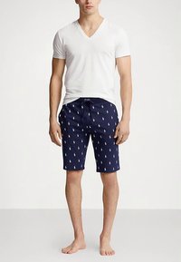 Biała koszulka z dekoltem w serek i granatowe szorty kąpielowe z małym białym wzorem w koniki. Szorty mają elastyczny pas z możliwością regulacji.