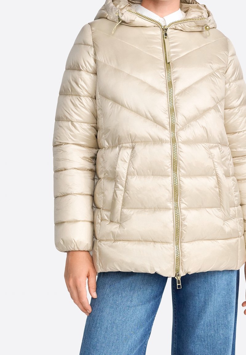 Beige puffer bunda s kapucí, s chevron prošíváním, zipem vpředu, dvěma bočními kapsami a zlatými kovovými detaily.