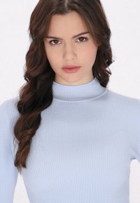 Maglione a collo alto a coste blu chiaro, con maniche lunghe, texture liscia e design aderente, caratterizzato da un alto colletto e un leggero splendore.