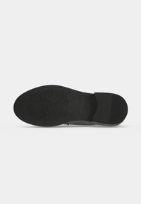 Semelle d'une chaussure noire avec une partie avant texturée et une partie talon rainurée sur un fond clair uni.
