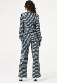 Gepatternde jumpsuit in zwart, blauw en crème met lange mouwen en uitlopende broekspijpen; bevat een geometrische print van driehoeken.