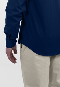 Marineblauw shirt met lange mouwen en knoopsluiting aan de manchetten, met een afgeronde zoom en een zachte textuur, gecombineerd met lichtbeige broeken.