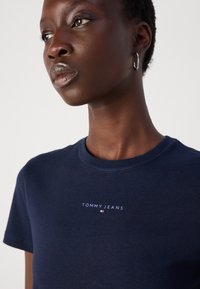 T-shirt in cotone blu navy con collo rotondo e maniche corte, con il logo bianco "TOMMY JEANS" stampato sul petto. Texture liscia.