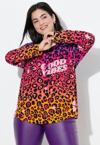Colorful leopard print shirt featuring shades of pink, orange, and purple with the text "GOOD VIBES" in white. Smooth, lightweight fabric.