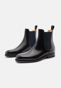 Botas Chelsea de cuero negro con paneles laterales de elasticidad, un acabado suave, puntera redonda y suela de goma negra. Presentan tiradores en la parte posterior.