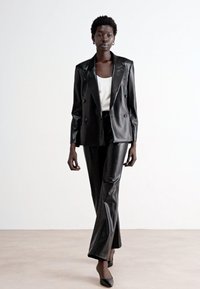Blazer doppiopetto in pelle nera abbinato a pantaloni coordinati. Il blazer presenta un colletto affilato e una silhouette strutturata.