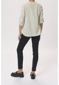 Green and white striped button-up shirt, roll-up sleeves, paired with black slim-fit jeans and chunky black loafers, set against a neutral backdrop.