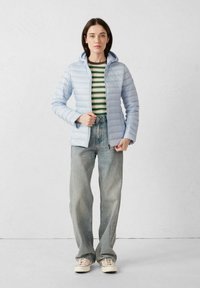 Lichtblauwe gewatteerde jas met capuchon, voorzien van een volledige rits en een aangesloten ontwerp. Draagt over een gestreept shirt en gecombineerd met wijd uitlopende spijkerbroeken.