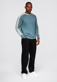 Sudadera azul claro con mangas raglán de un azul pálido en contraste, combinada con pantalones negros y zapatillas blancas. Textura suave, ajuste casual.