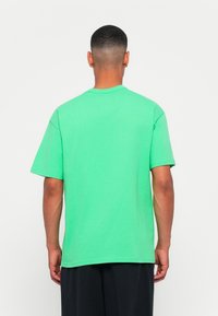 Tricou din bumbac verde, cu mâneci scurte, guler rotund și o croială lejeră. Textură fină, fără modele, design simplu.