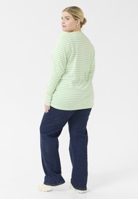 Lichtgroene langemouwen shirt met witte strepen, gecombineerd met donkerblauwe jeans en lichte schoenen. Eenvoudig ontwerp, casual pasvorm.
