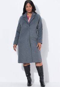 Cappotto grigio in misto lana con colletto a punta, maniche lunghe e taglio dritto, abbinato a stivali neri in pelle al ginocchio.