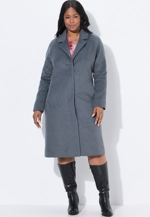 Cappotto grigio in misto lana con colletto a punta, maniche lunghe e taglio dritto, abbinato a stivali neri in pelle al ginocchio.