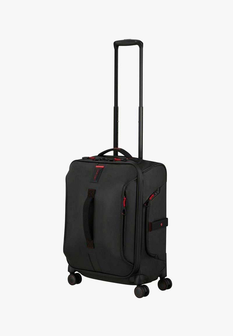 Valise noire rigide à parois souples avec des accents de fermeture éclair rouges, poignée télescopique, poche latérale et quatre roues pivotantes pour une mobilité facile.