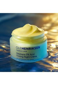 Barattolo giallo della Crema Notturna Rassodante Dewtopia 5% Acid di Ole Henriksen, con una consistenza cremosa liscia e un'etichetta testuale in blu scuro.