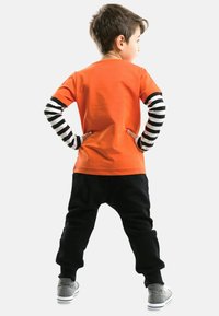 Orangenes T-Shirt, schwarze Sweatpants mit lässiger Passform, gestreifte langärmlige Bluse in Schwarz und Weiß, graue Sneaker. Einfaches und lässiges Outfit.