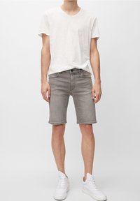Pantalones cortos de mezclilla gris con un ajuste informal, diseño de cinco bolsillos y un acabado ligeramente desgastado, combinados con una camiseta blanca de manga corta y zapatillas blancas.