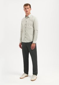 Lange mouwen blouse van een licht crèmekleurige stof met een klein groen bloemenpatroon, gecombineerd met donkere broek en witte sneakers.