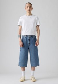Culottes de mezclilla de color azul claro con diseño de corte recto, combinados con una camiseta blanca lisa y zapatillas beige. Presentan un cierre de botones a la vista.
