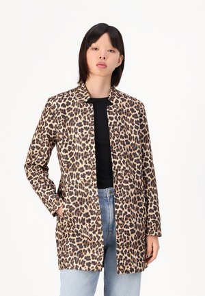 Giacca con stampa leopardata caratterizzata da un design senza colletto, maniche lunghe e due tasche laterali, realizzata in tessuto testurizzato. Indossata sopra un top nero.