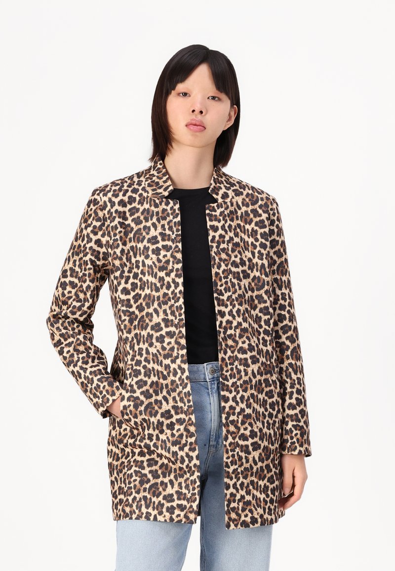 Jachetă cu imprimeu de leopard, care prezintă un design fără guler, mâneci lungi și două buzunare laterale, realizată dintr-un material texturat. Pur tată pe un top negru.