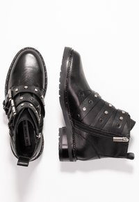 Černé kožené kotníkové boty s přezkami, metalickými hřebíky, zipem a texturovanými detaily po stranách. Silné, odolné podrážky.