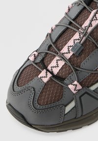 Sport shoe with a grey synthetic upper, brown mesh panels, pink laces, and black outsole; features textured surfaces and design accents.